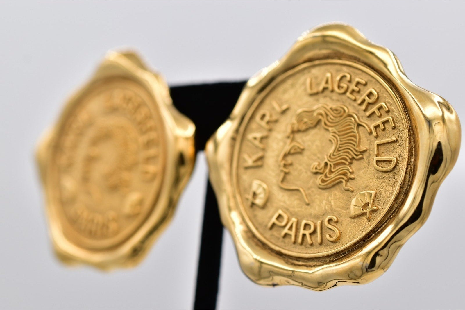 Gold earrings with 'Karl Lagerfeld Paris' branding on a gray background