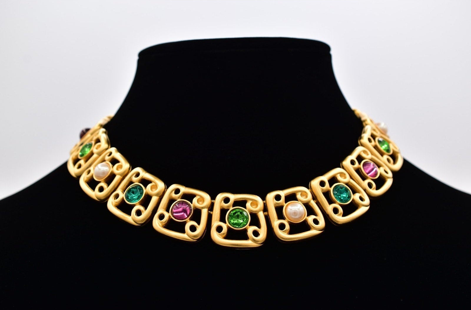 Gold necklace with colored stones on a black mannequin against a white background