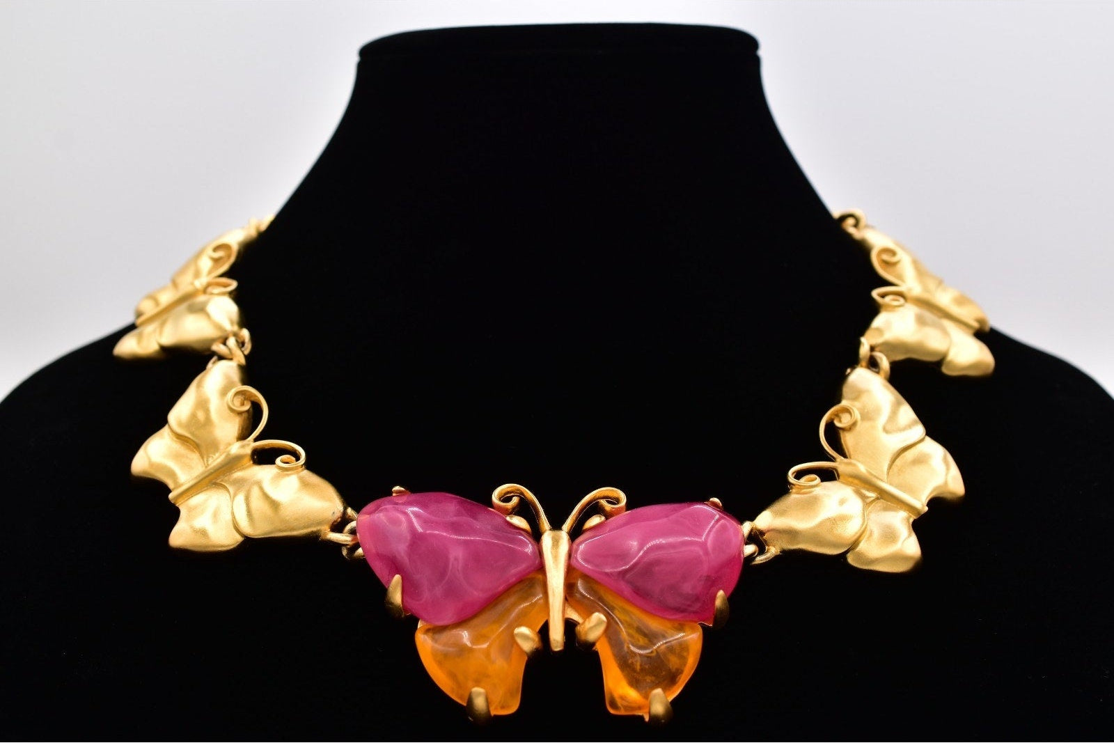 Gold butterfly necklace with pink center on a black mannequin against a white background