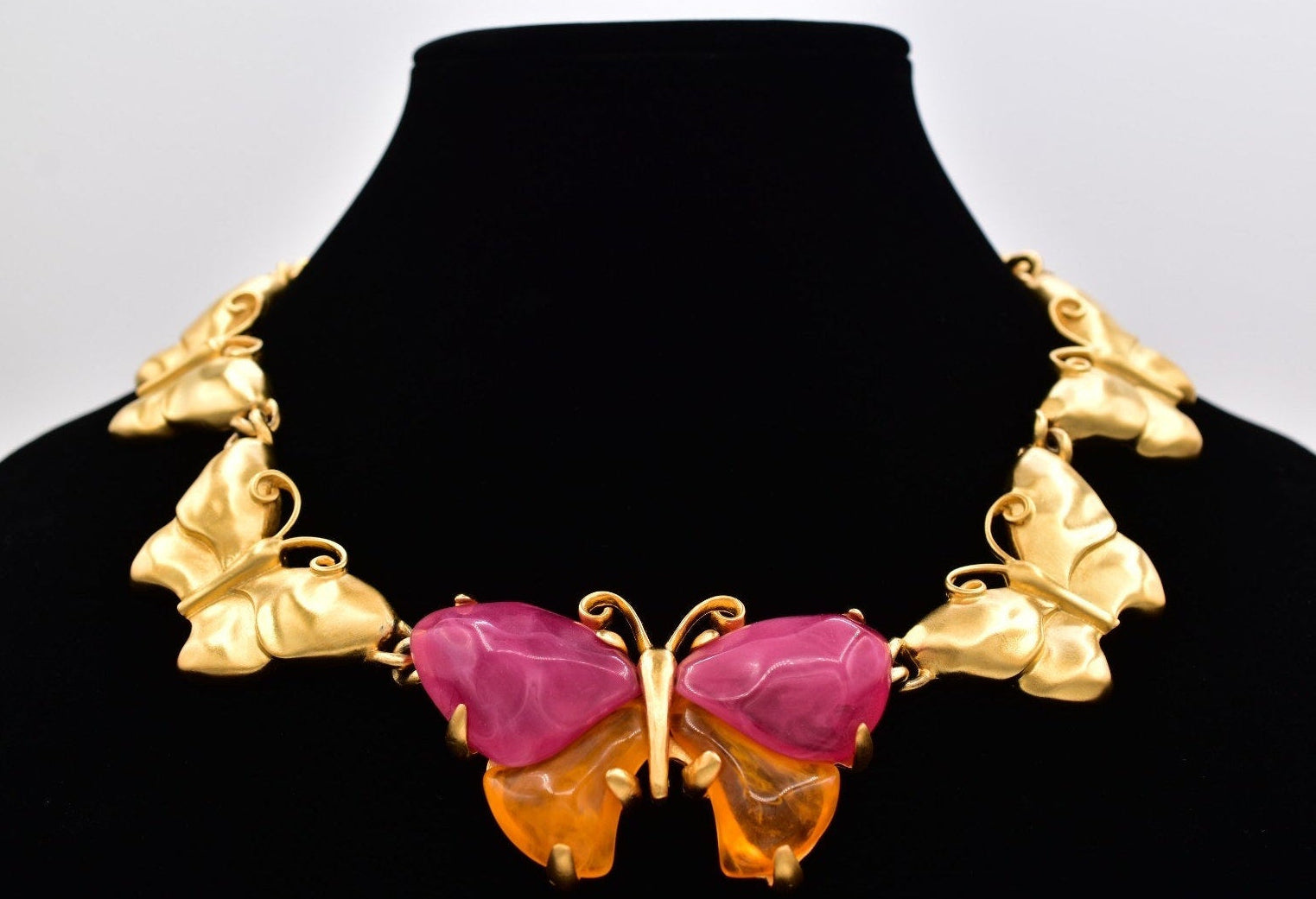 Vintage Givenchy gold butterfly necklace with pink and orange lucites on a black mannequin against a white background