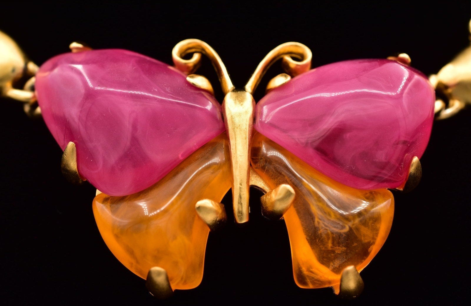 Close up of a vintage Givenchy gold butterfly necklace with pink and orange lucites on a black mannequin against a black background.