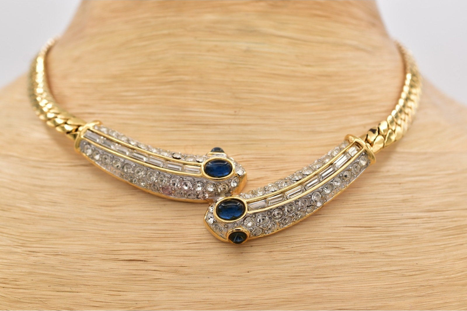 Gold necklace with blue stones and clear stones on a mannequin neck.