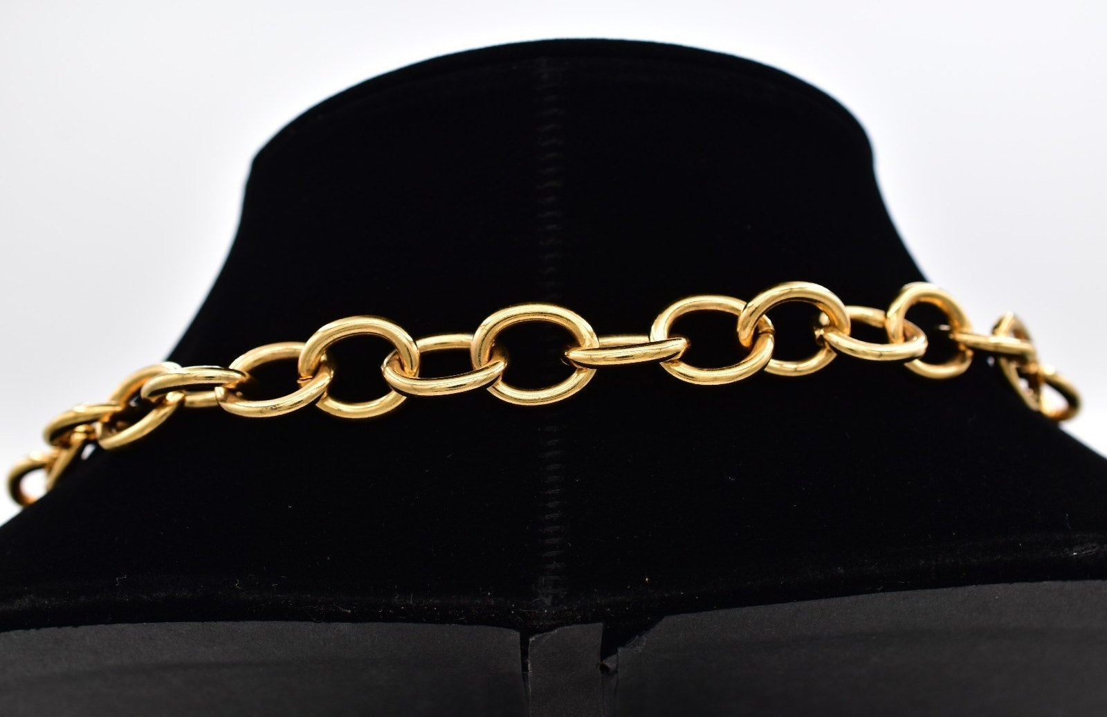 Gold chain necklace on a black mannequin head against a white background