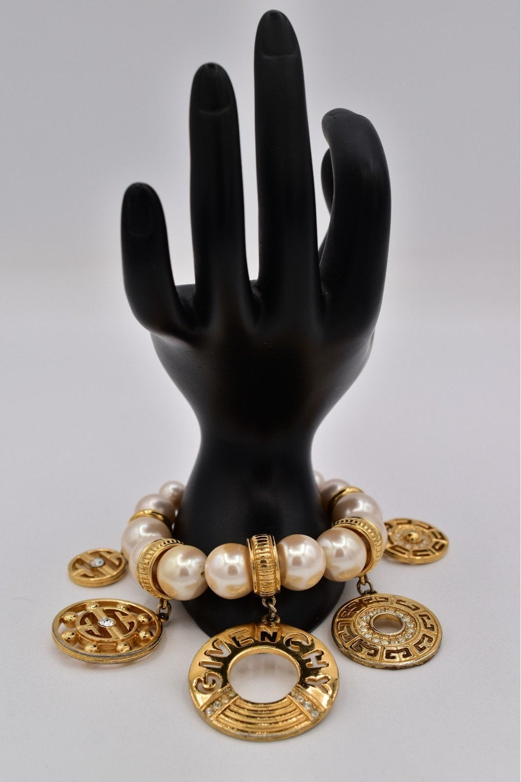 Black mannequin hand with gold and pearl bracelet on a gray background