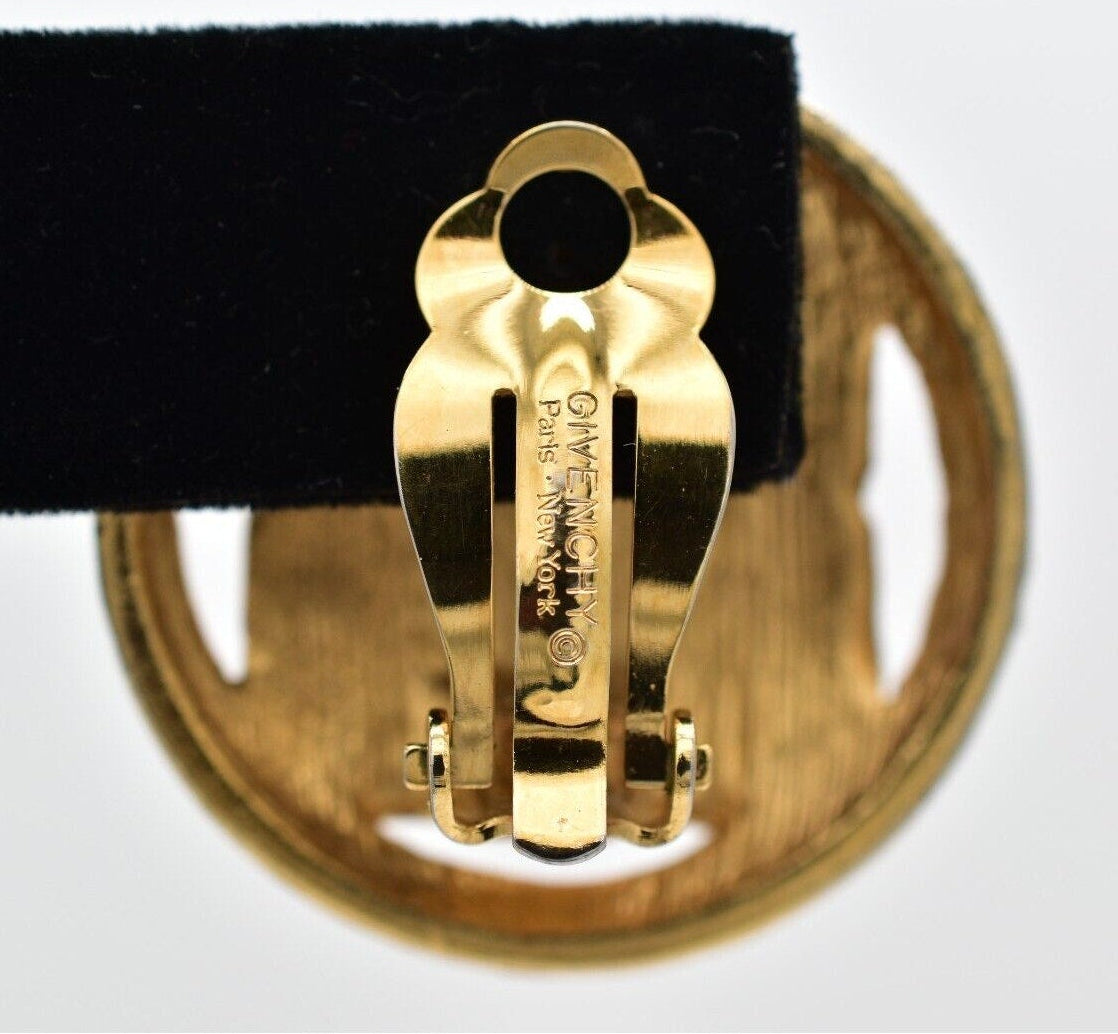 Gold earring on a black belt against a white background