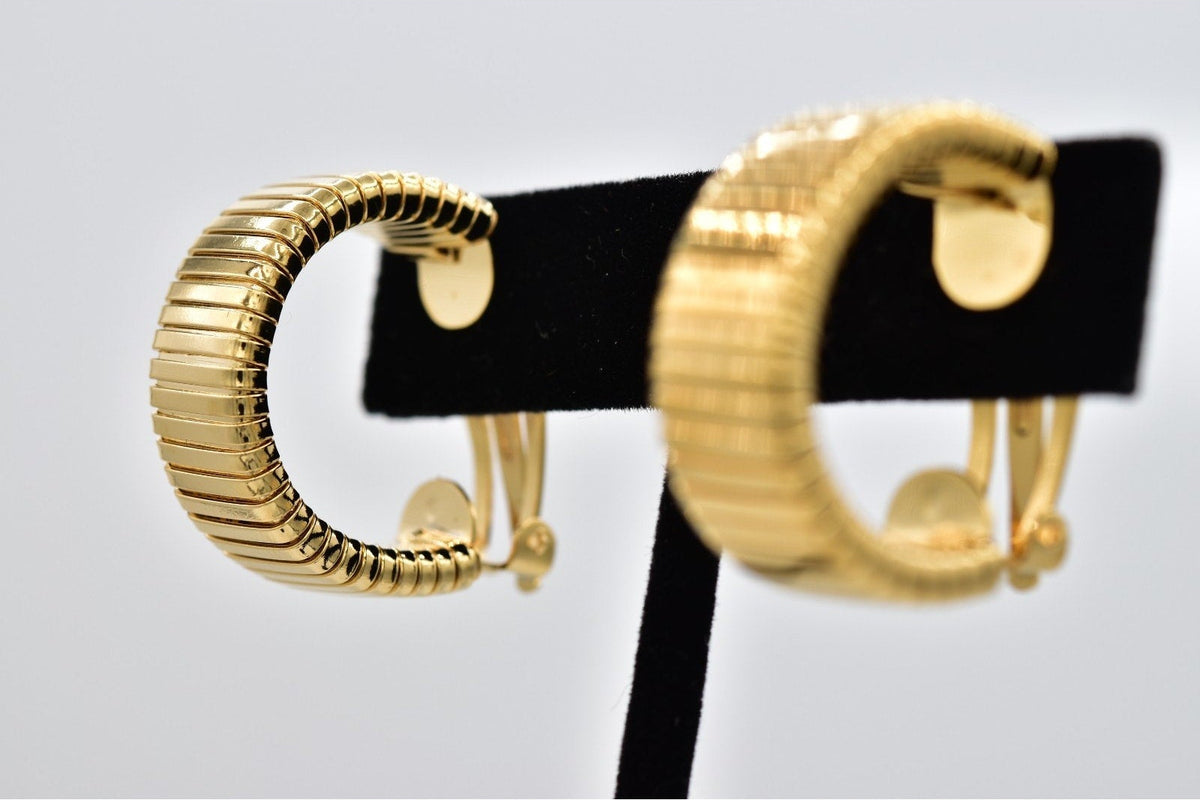 A pair of gold hoop earrings with a textured, ribbed snake-style band design, displayed on a black jewelry stand against a light gray background.