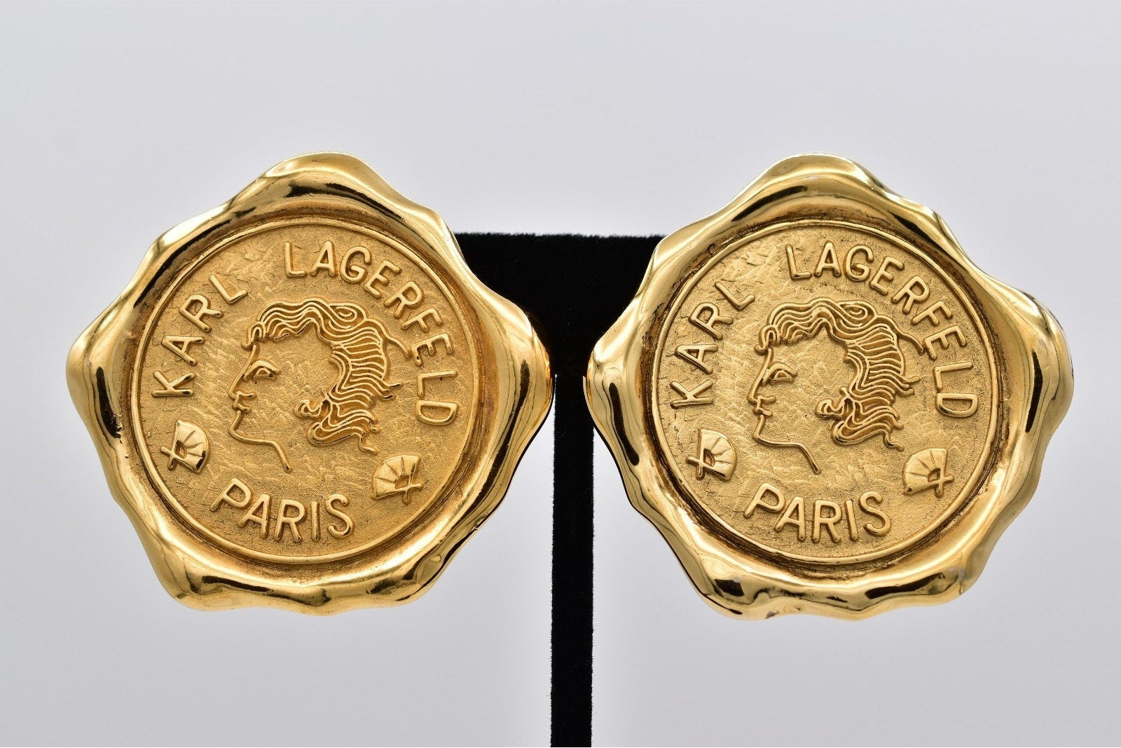 Gold Karl Lagerfeld Paris earrings on a gray background