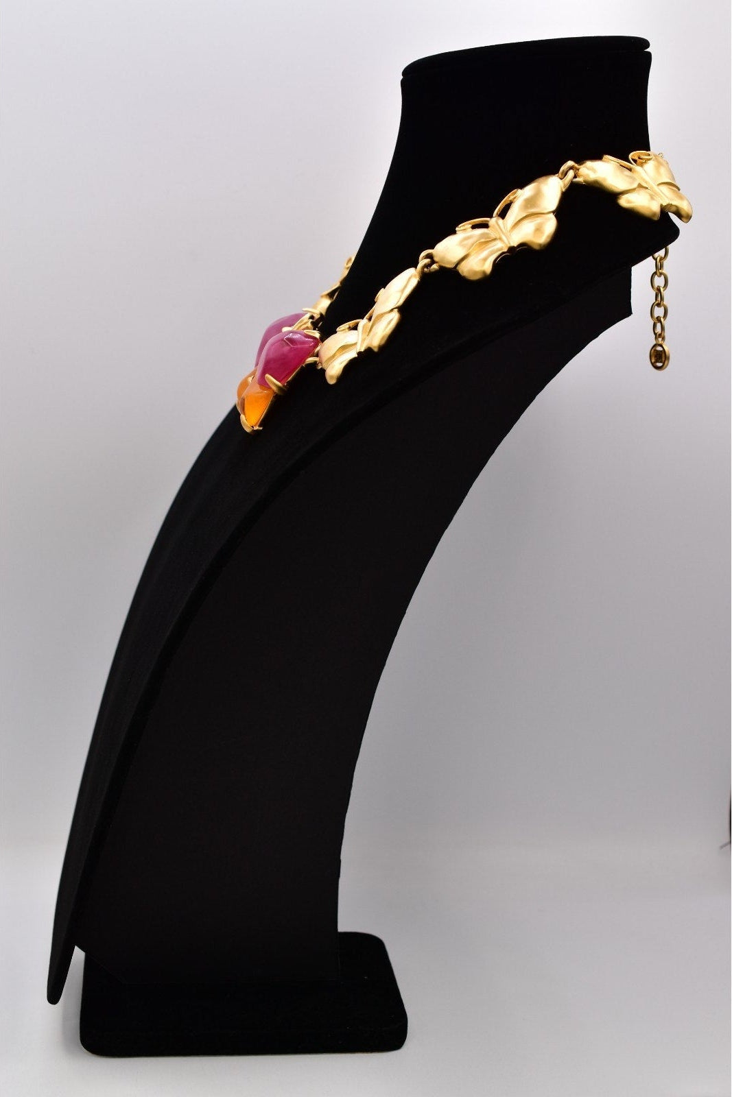 Side view of a vintage Givenchy gold butterfly necklace with pink and orange lucites on a black mannequin against a white background.