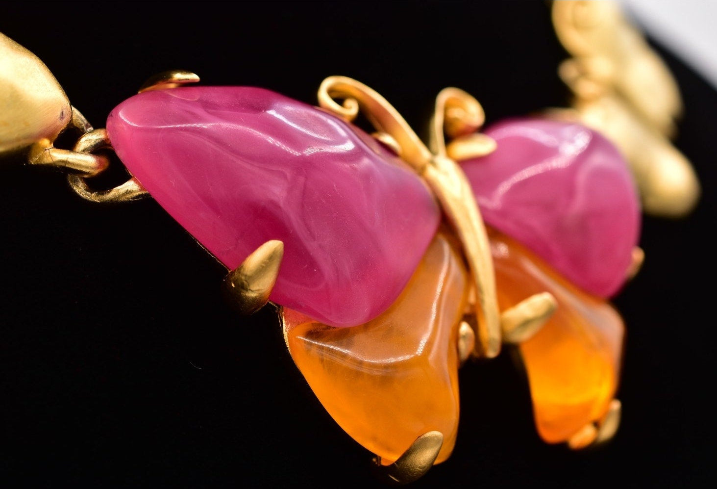 Angled view of a vintage Givenchy gold butterfly necklace with pink and orange lucites on a black mannequin against a white background.