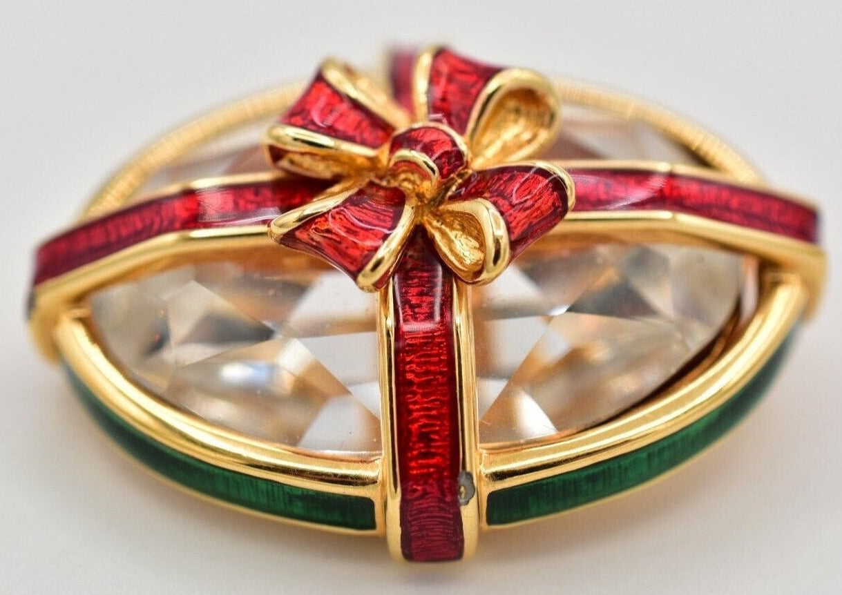 A vintage Swarovski crystal pin with a sparkling central crystal wrapped in a red enamel bow with gold-tone edges.
