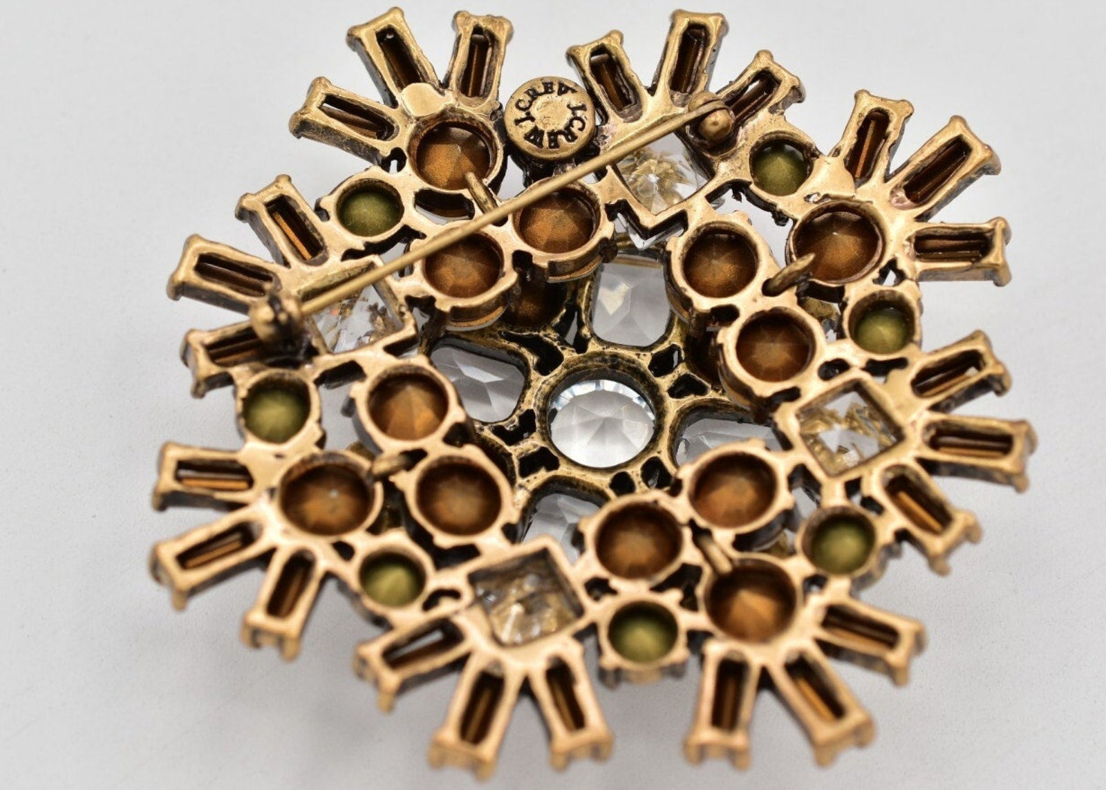 Back of a gold brooch with embedded gemstones on a light gray background