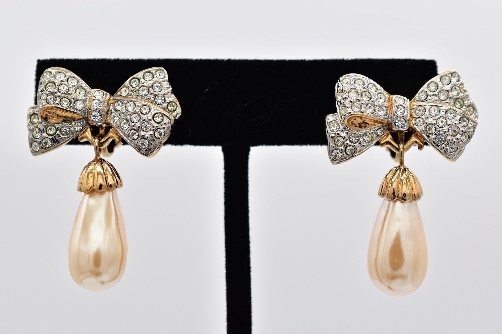 Bow-shaped earrings with pearl drops on a black and white stand.
