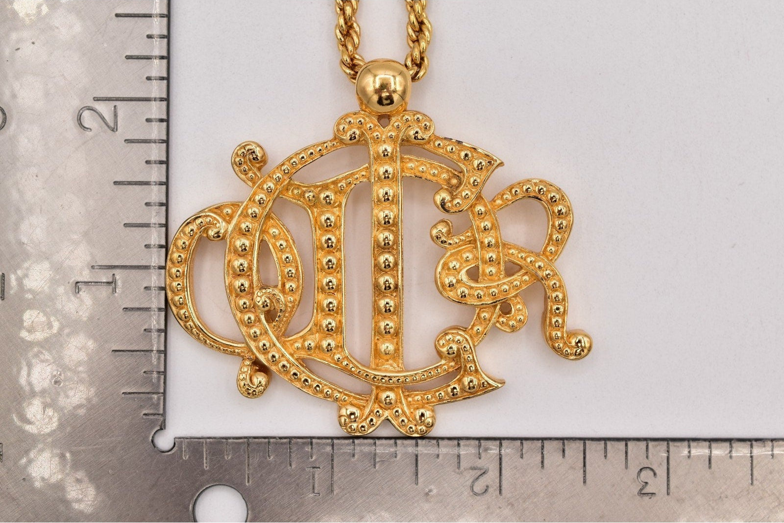 Gold necklace with a decorative pendant on a white background with a ruler for scale.