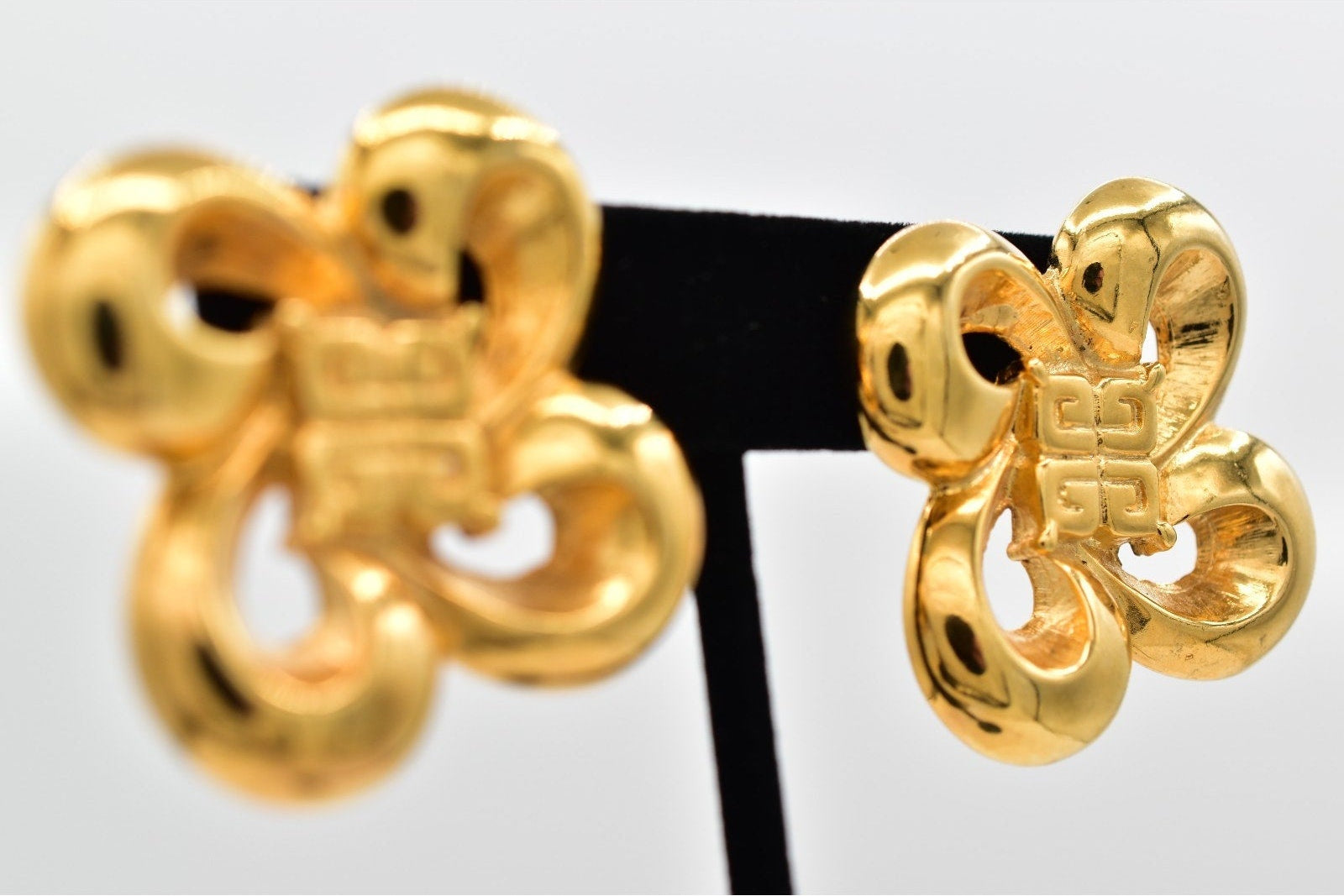 Gold earrings on a black stand with a white background