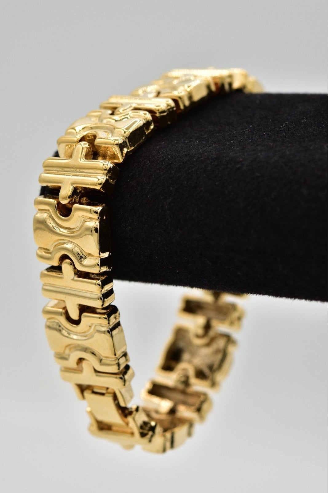 A gold-toned puzzle-link bracelet displayed on a black velvet jewelry stand against a light gray background.
