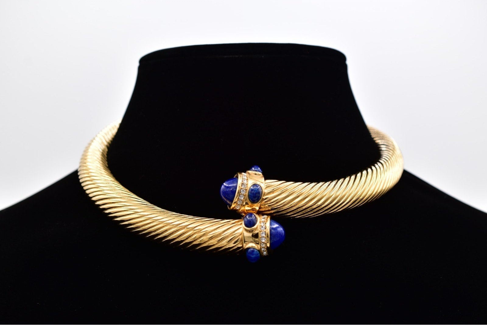 Gold necklace with blue accents on a black mannequin against a white background