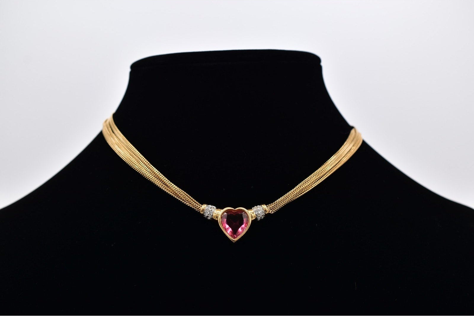 Gold necklace with a heart-shaped pink gemstone on a black mannequin against a white background