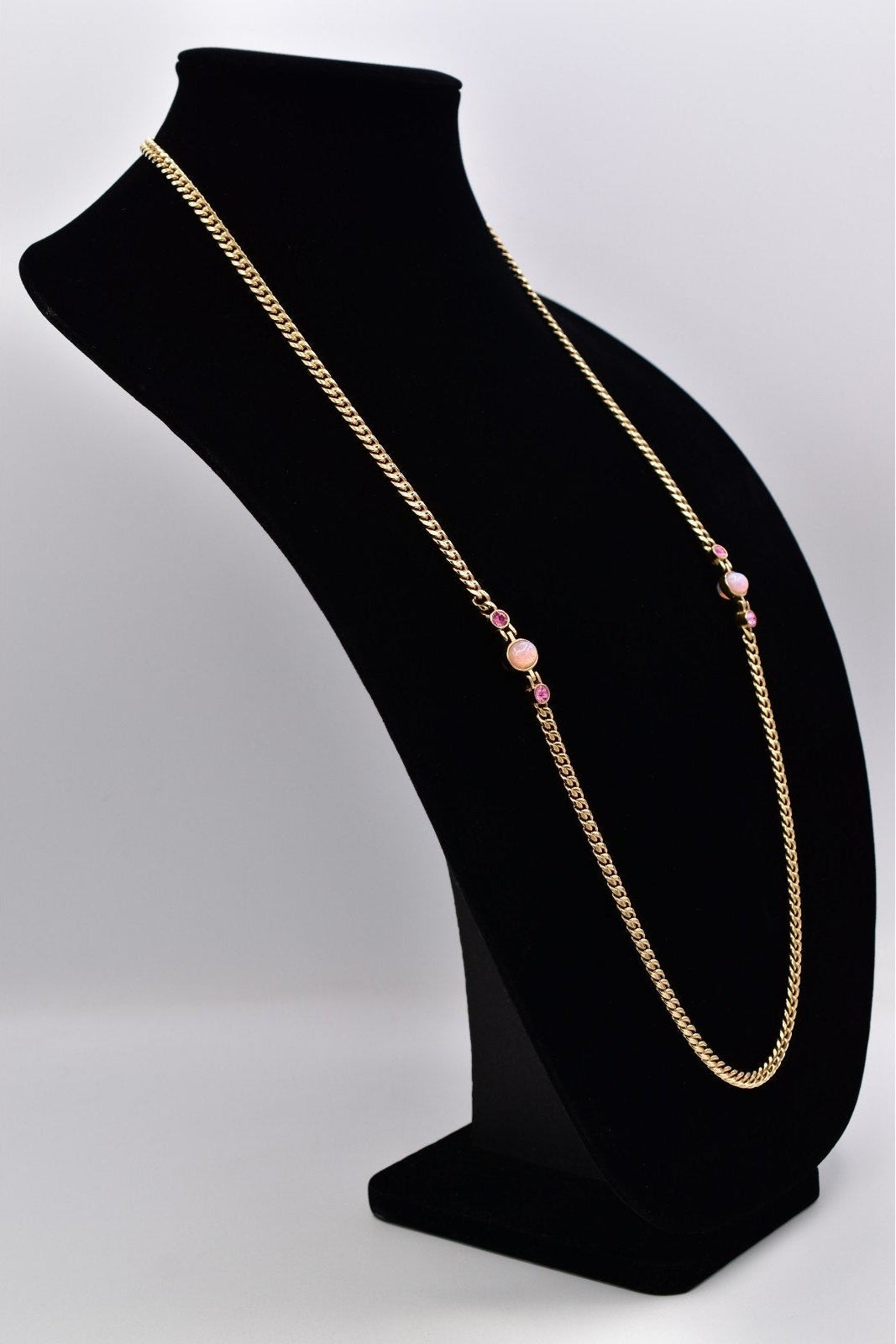 A gold chain necklace with small pink beads, displayed on a black jewelry bust against a light gray background.