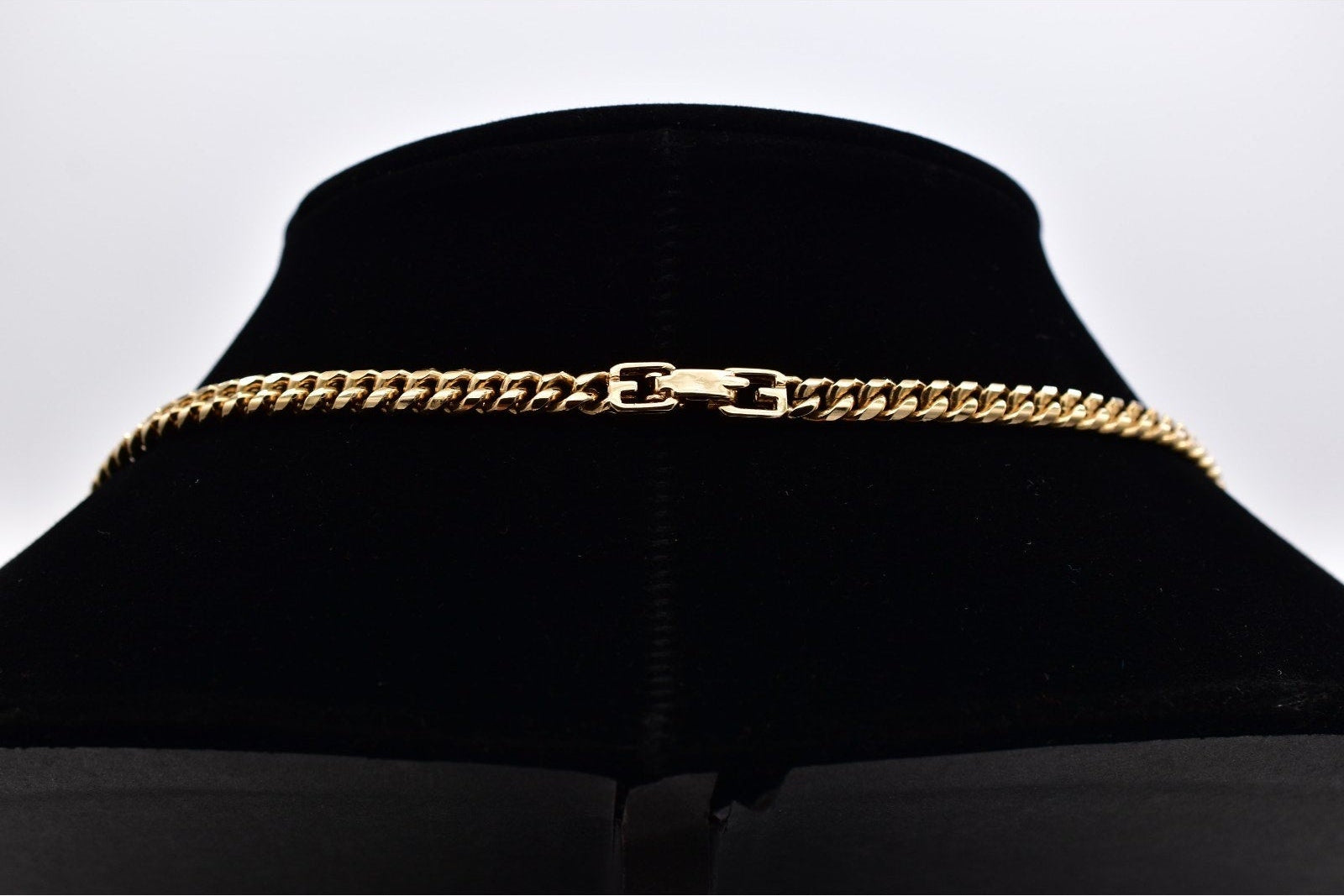 A gold-toned curb chain necklace displayed on a black velvet jewelry bust against a light gray background.