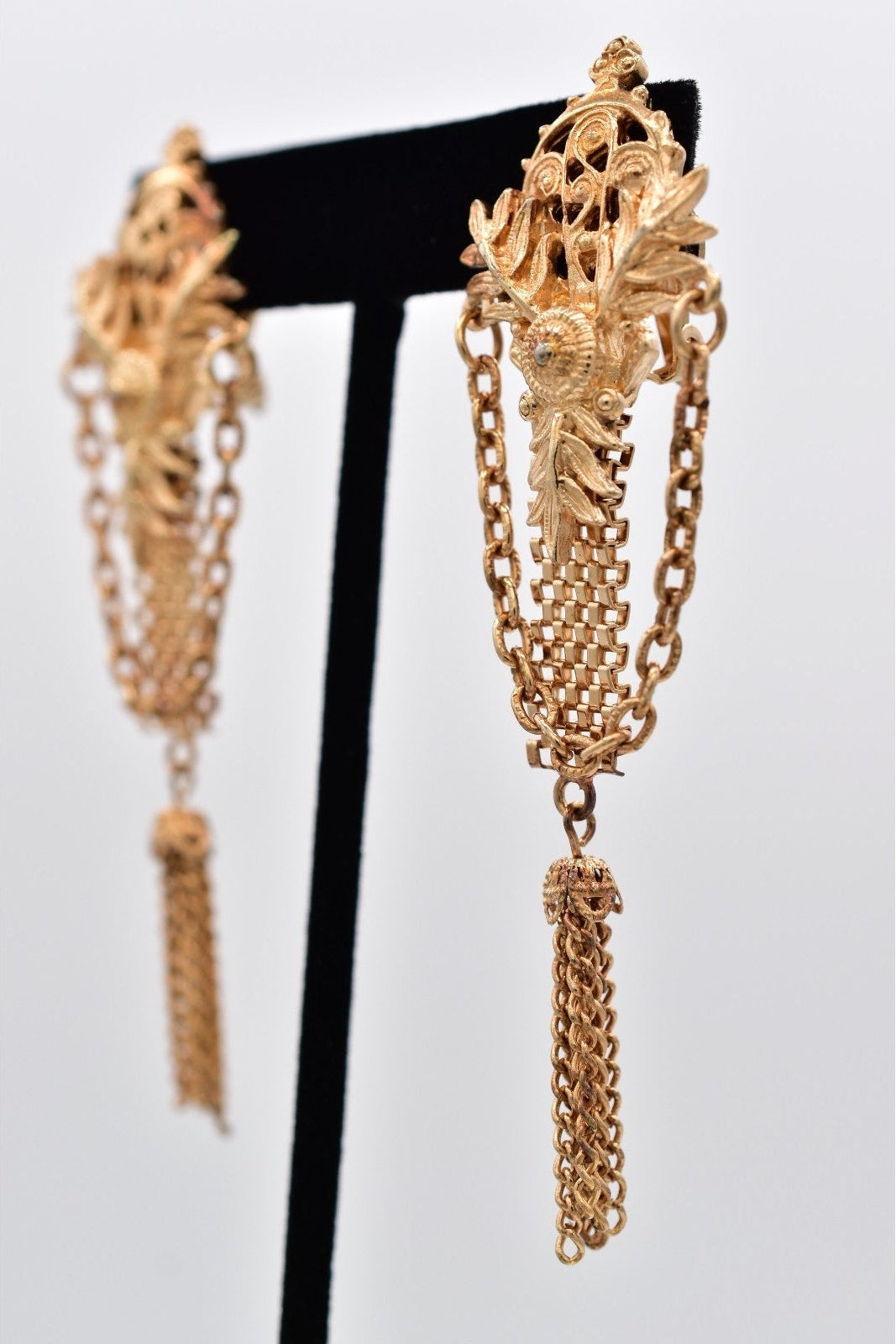 Gold chain earrings on a black stand against a light gray background