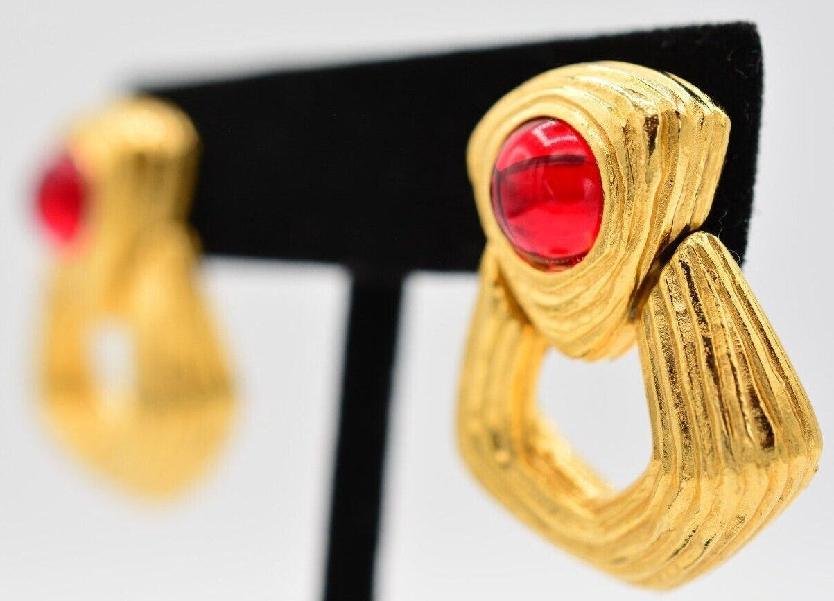 Gold earrings with red Cabochons on a black stand against a light gray background