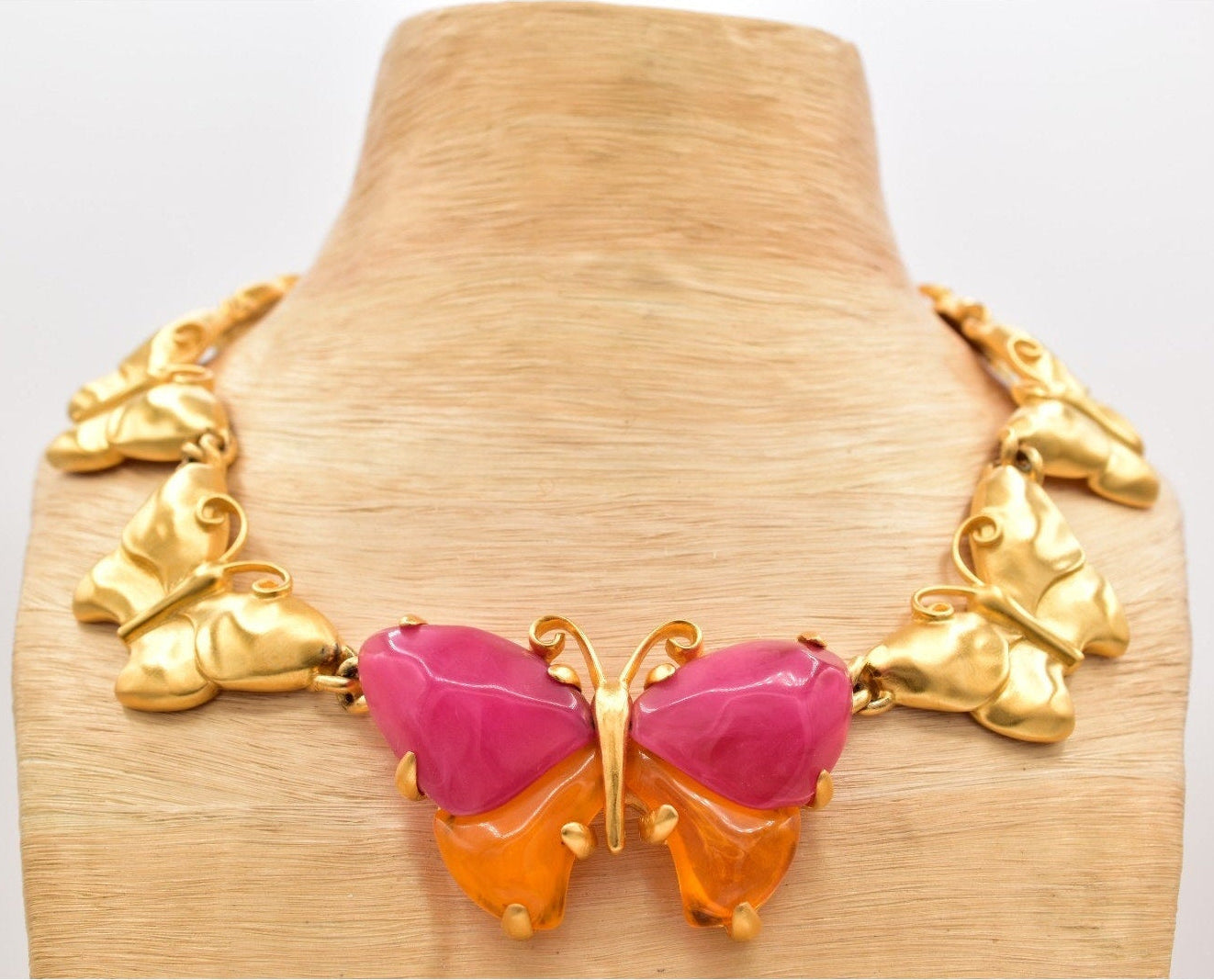 Gold butterfly necklace with pink and orange center on a wooden mannequin.