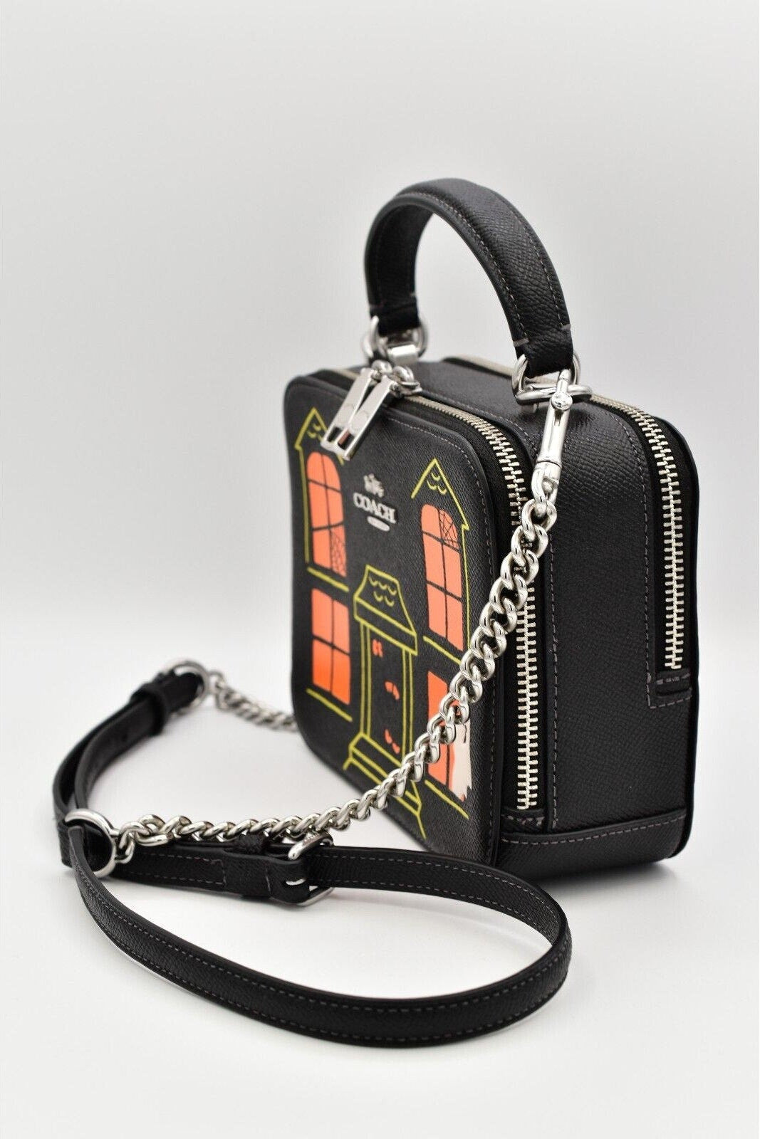 A black faux-leather handbag with a top handle and silver chain strap, featuring a printed Doctor Who TARDIS house design on the front.