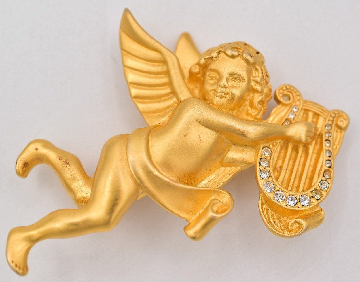 Gold cherub brooch with a harp on a light gray background