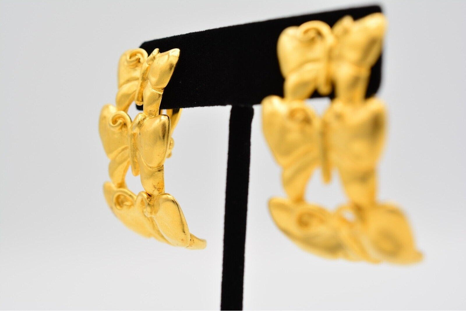 A pair of textured gold hoop earrings displayed on a black jewelry stand against a light gray background.
