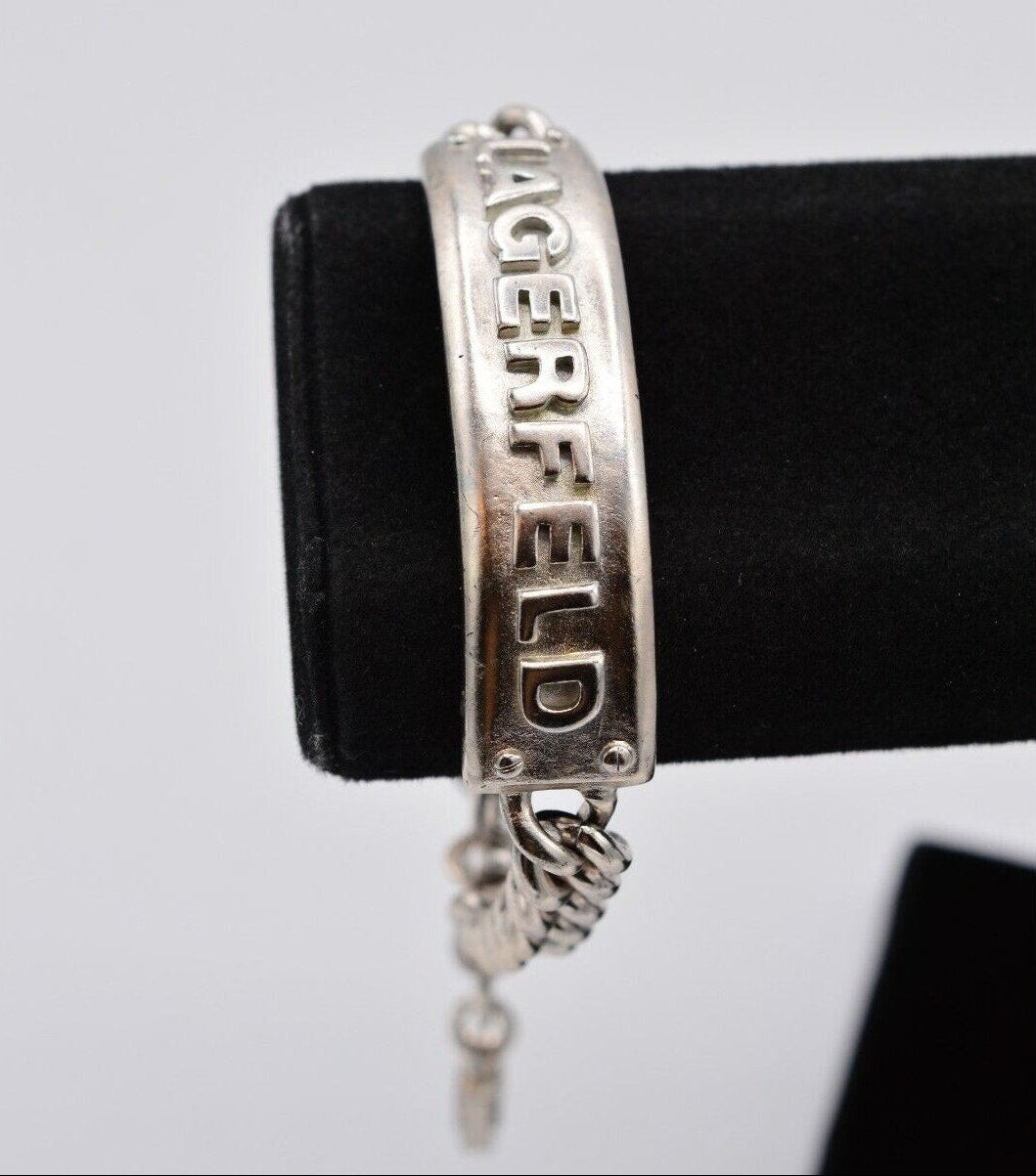 Silver bracelet with 'Lagerfeld' branding on a black stand against a light gray background