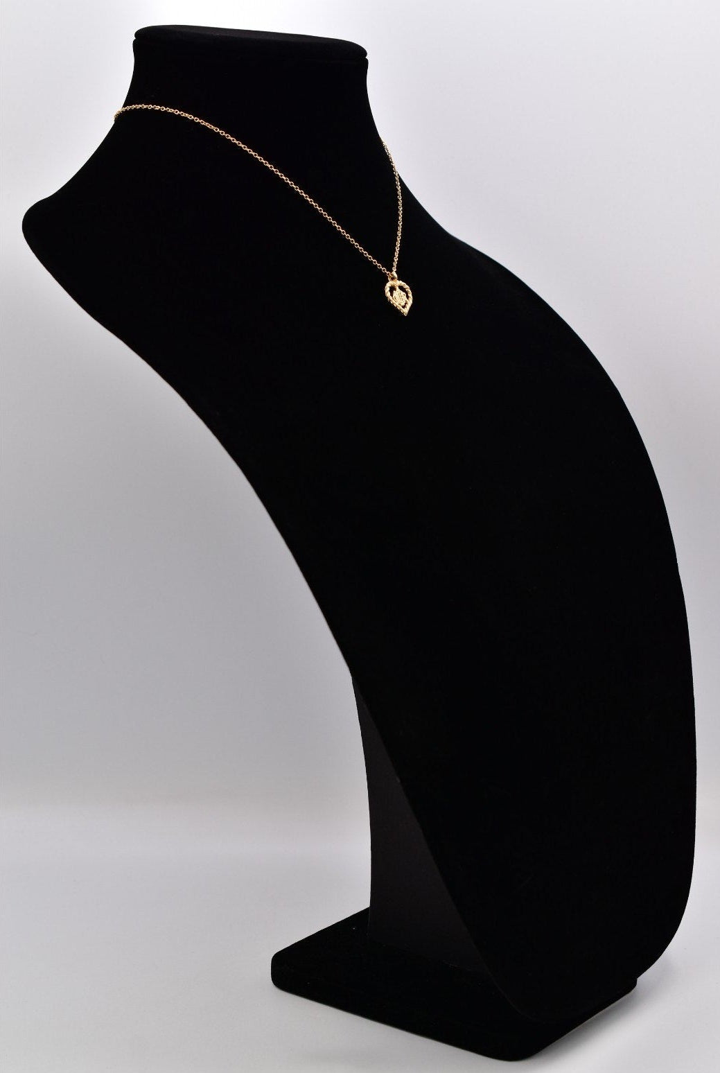 Black velvet jewelry display stand with a gold necklace on a white background