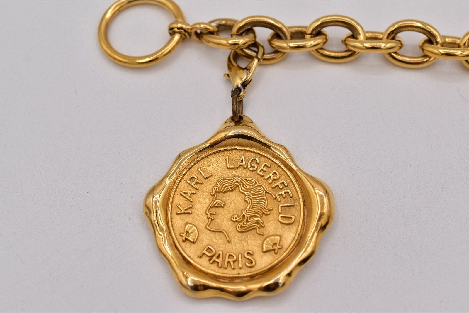 Gold chain with a Karl Lagerfeld Paris pendant on a gray background