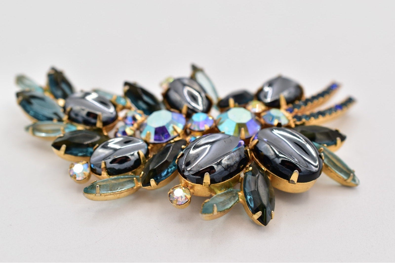 Multicolored gemstone brooch with gold accents on a light gray background