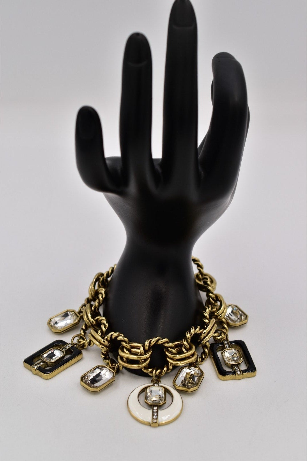 Black mannequin hand with a gold and crystal bracelet on a gray background