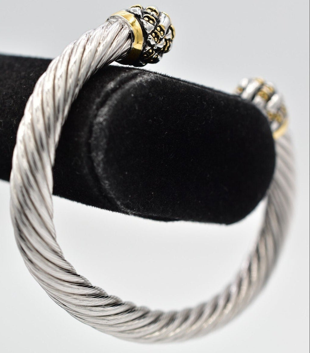 Silver cable-style bracelet with a gold clasp on a black velvet stand.