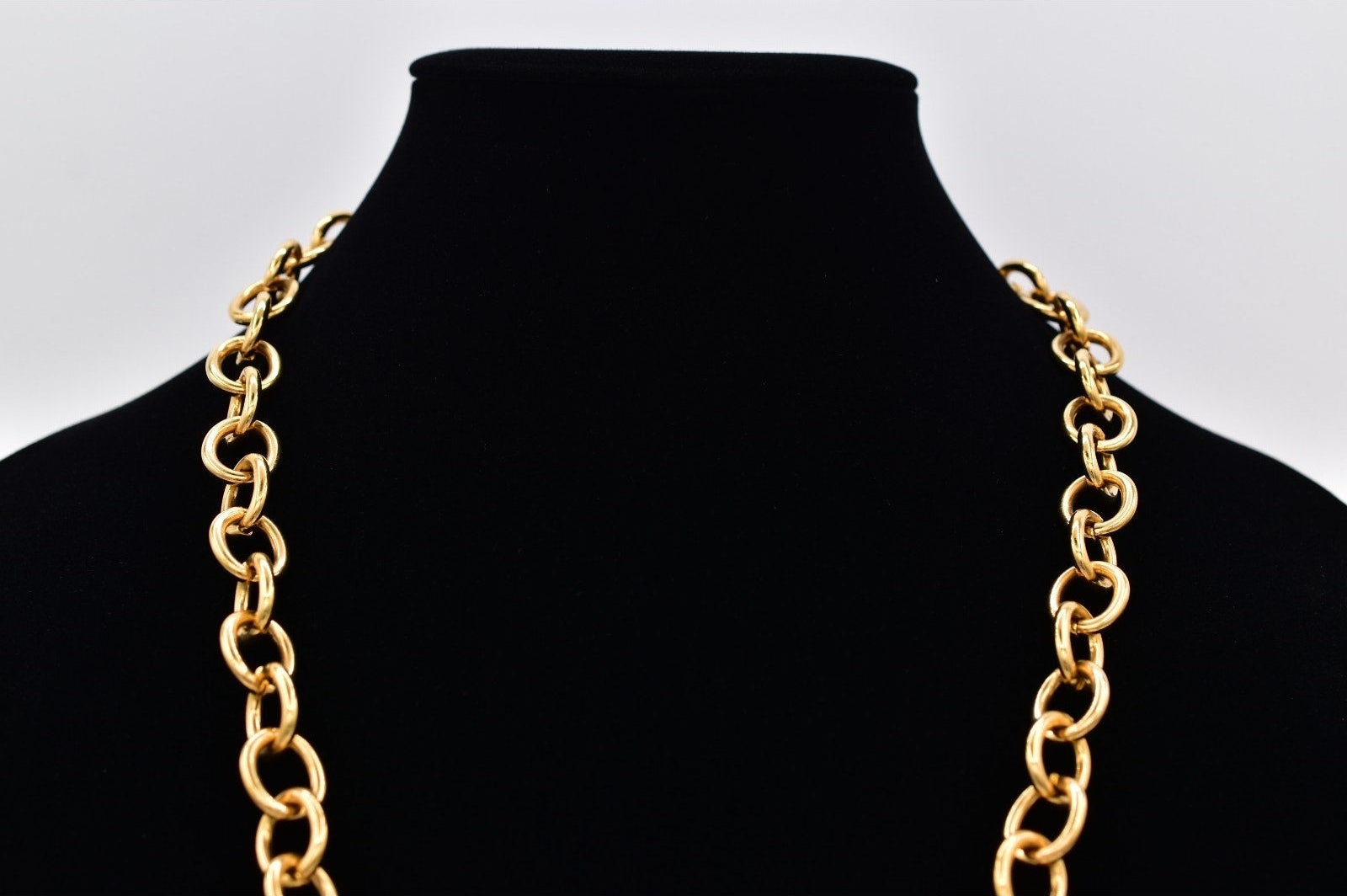 Gold chain necklace on a black mannequin bust against a white background
