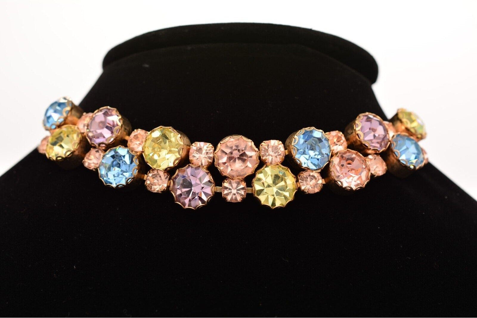 Multicolored gemstone choker on a black stand with a white background