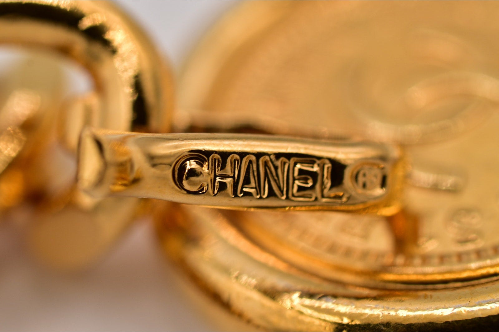 Close-up of a gold Chanel earring with the brand name engraved.