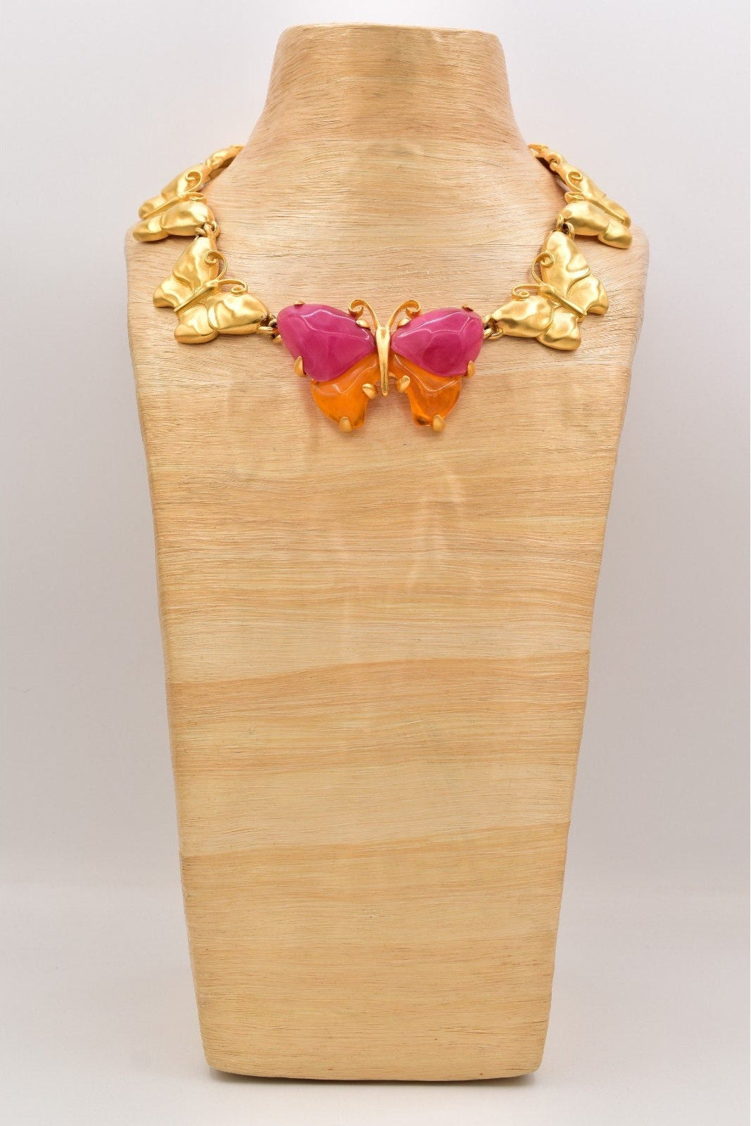 Butterfly-shaped necklace with gold, pink, and orange design on a wooden mannequin.
